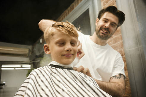 Lächelnder Friseur bürstet die Haare eines Kunden im Friseursalon - MRPF00019