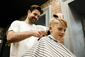 Lächelnder Friseur, der einem Kunden mit einem elektrischen Rasiermesser die Haare schneidet - MRPF00021