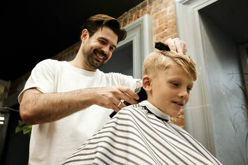 Lächelnder Friseur, der einem Kunden mit einem elektrischen Rasiermesser die Haare schneidet - MRPF00021