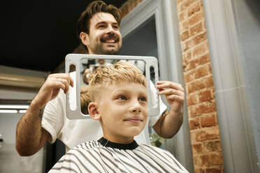 Glückliche Friseurin zeigt dem Kunden im Spiegel den Haarschnitt im Salon - MRPF00023