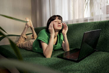 Depressiver Freiberufler auf dem Sofa liegend mit Laptop zu Hause - MBLF00145