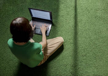 Freiberufler, der auf einem Teppich sitzt und einen Laptop zu Hause benutzt - MBLF00150