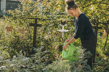 Lächelnde Frau, die Pflanzen im Garten gießt - ADF00260