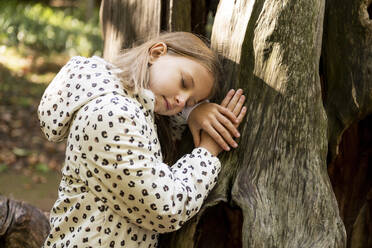 Mädchen lehnt mit geschlossenen Augen an einem Baumstamm im Park - LMCF00672