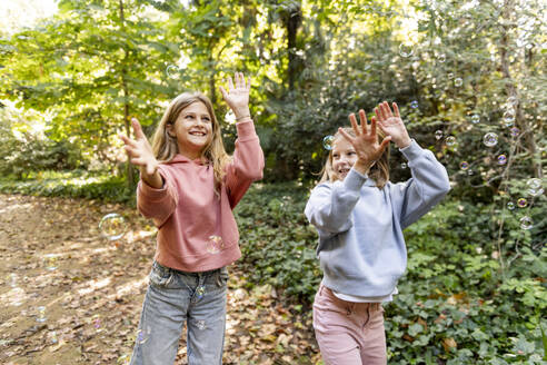 Glückliche Mädchen spielen mit Seifenblasen im Park - LMCF00680