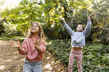 Smiling girls playing with bubbles in park - LMCF00681