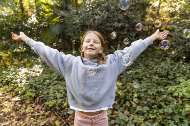 Smiling girl with arms outstretched standing in park - LMCF00683