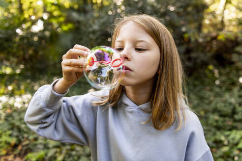 Girl blowing bubble with wand in park - LMCF00686