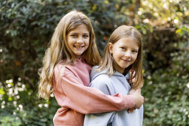 Happy girl standing with arm around friend in park - LMCF00687