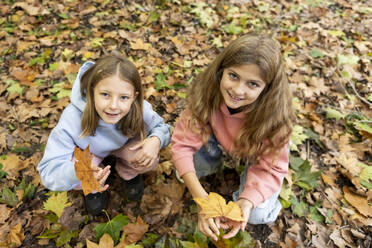 Smiling girls with maple leaves crouching in park - LMCF00691