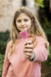 Smiling girl holding heart shaped lollipop candy - LMCF00695