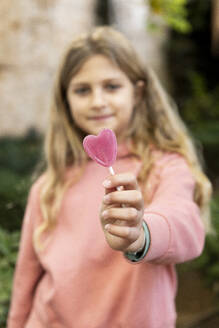 Lächelndes Mädchen hält herzförmige Lollipop-Bonbons - LMCF00695