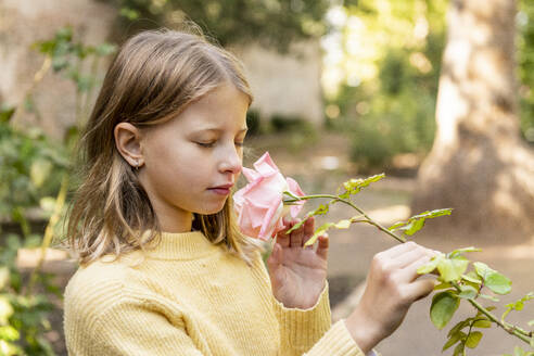 Mädchen mit geschlossenen Augen riecht an rosa Rosenblüten im Park - LMCF00700