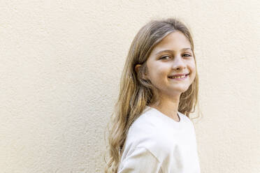 Happy girl with long hair standing in front of wall - LMCF00701