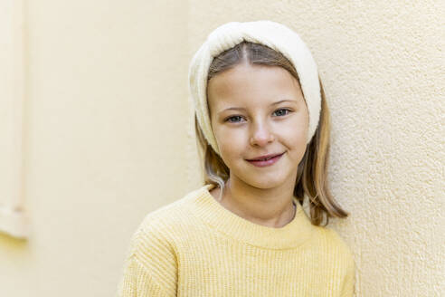 Smiling girl wearing headband in front of wall - LMCF00704
