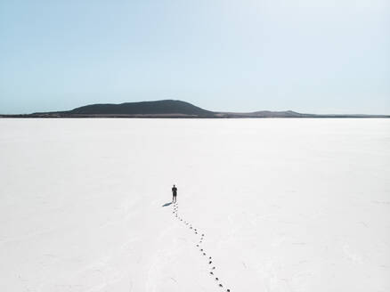 Aerial view a person standing on an empty salt flat with footprints leading up to the person, South Australia. - AAEF24011