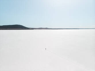 Aerial view a person standing on an empty salt flat with footprints leading up to the person, South Australia. - AAEF24012