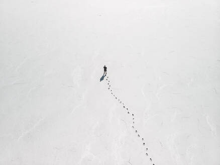 Aerial view a person standing on an empty salt flat with footprints leading up to the person, South Australia. - AAEF24014