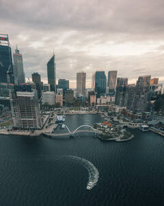 Panoramic aerial view of Elisabeth Quay at sunset with a boat driving and the skyscrapers surrounding the harbour, Perth, Western Australia. - AAEF24019