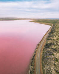 Aerial view of the pink Hutt Lagoon with a road going along the salt lake, Western Australia. - AAEF24028