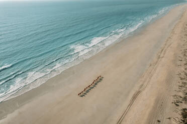 Aerial view of camels walking on a beach with people riding on their back and the ocean located their left, Broome, Western Australia. - AAEF24040