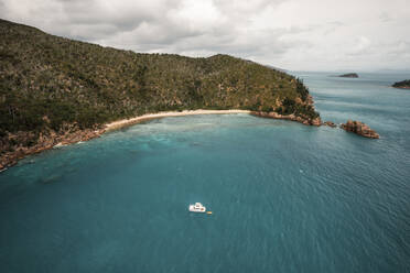 Aerial view of Blue Pearl Bay with a boat in the turquoise water and green hills behind the beach, Hayman Island, Australia. - AAEF24043