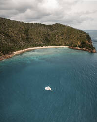 Aerial view of Blue Pearl Bay with a boat in the turquoise water and green hills behind the beach, Hayman Island, Australia. - AAEF24044