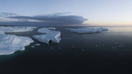 Aerial drone view a iceberg with a cave surrounded by a red sailing boat, Ilulissat, Greenland. - AAEF24163