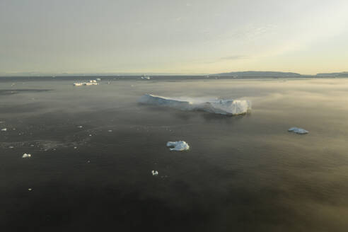 Drohnenaufnahme eines riesigen Eisbergs im Nebel bei sanftem Morgenlicht in Ilulissat, Grönland, Arktis. - AAEF24180