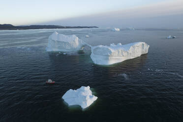 Aerial drone view a huge iceberg with an arch surrounded by a red boat, Ilulissat, Greenland, Arctic. - AAEF24182