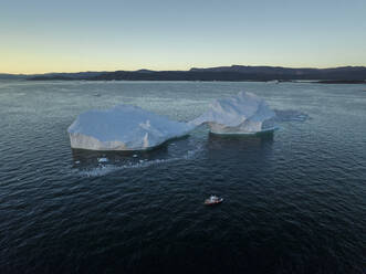 Aerial drone view a huge iceberg with an arch surrounded by a red boat, Ilulissat, Greenland, Arctic. - AAEF24184