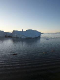 Drohnenaufnahme von Kajaks in der Eisfjordlagune von Ilulissat, vorbei an riesigen Eisbergen, Grönland, Arktis. - AAEF24194