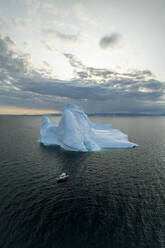 Aerial drone view of a red boat in front of a huge iceberg in Ilulissat, Greenland, Arctic. - AAEF24201