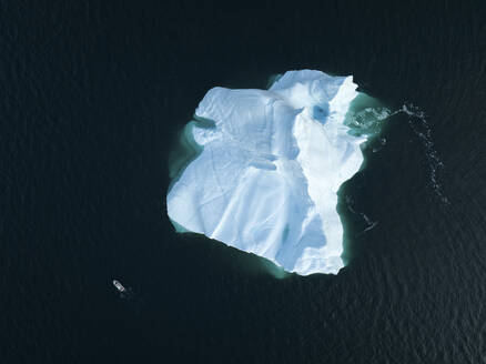 Aerial top-down drone view of a boat in front of a gigantic iceberg in Ilulissat, Greenland, Arctic. - AAEF24202