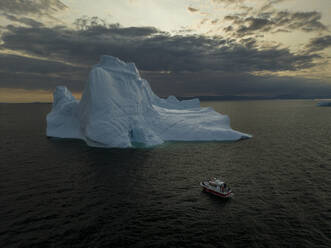 Aerial drone view of a red boat in front of a huge iceberg in Ilulissat, Greenland, Arctic. - AAEF24203