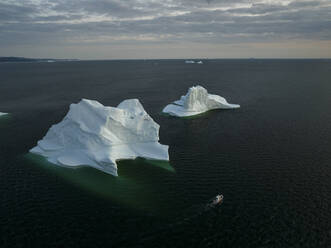 Aerial drone view of gigantic icebergs and a boat in Ilulissat at dawn, Greenland, Arctic. - AAEF24205