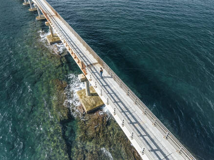 Luftaufnahme einer Frau, die auf der Vivara-Brücke spazieren geht, die das Naturschutzgebiet der Insel Vivara mit der Insel Procida verbindet, Archipel der Flegree-Inseln, Neapel, Kampanien, Italien. - AAEF24420