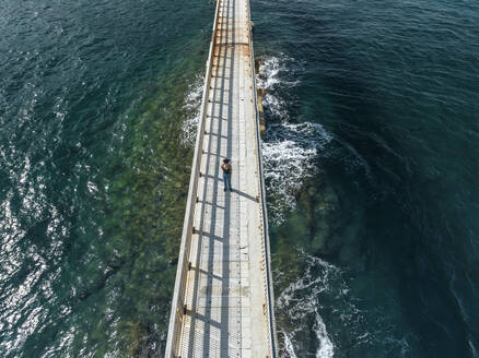 Luftaufnahme einer Frau, die auf der Vivara-Brücke spazieren geht, die das Naturschutzgebiet der Insel Vivara mit der Insel Procida verbindet, Archipel der Flegree-Inseln, Neapel, Kampanien, Italien. - AAEF24424