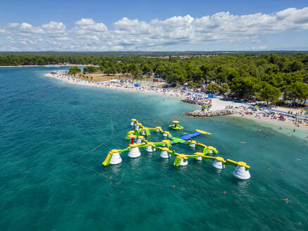 Aerial view of a kids playground on water along the coastline with people on the beach at Hidrobaza promenade near Pula, Istria, Croatia. - AAEF24591