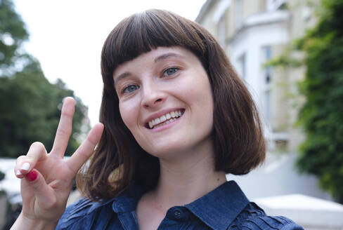 Happy young woman gesturing peace sign - ASGF04740