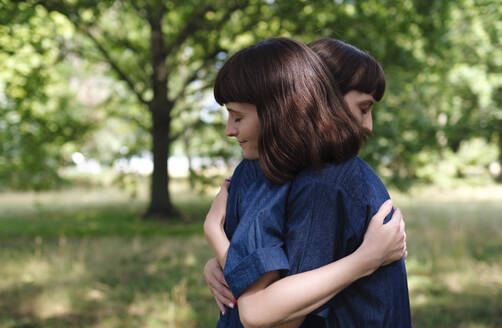 Smiling twin sisters hugging each other in park - ASGF04759