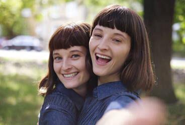 Happy twin sisters taking selfie in park - ASGF04767