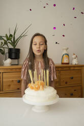 Glückliches Mädchen bläst Kerzen auf Geburtstagskuchen zu Hause aus - LESF00507