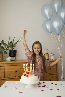 Fröhliches Mädchen hält Luftballons und feiert Geburtstag mit Kuchen zu Hause - LESF00509