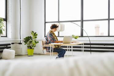 Young graphic designer working on laptop sitting at desk in office - MDOF01611