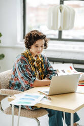 Young illustrator using laptop sitting at desk in office - MDOF01612