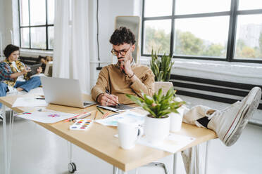 Thoughtful illustrator working with feet up at desk in office - MDOF01621