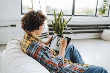 Junge Illustratorin arbeitet an einem Grafiktablett auf dem Sofa im Büro - MDOF01623