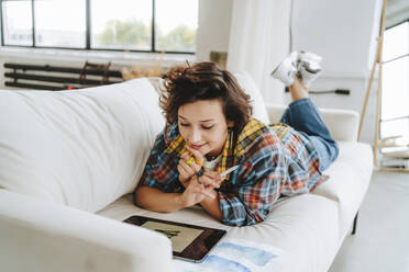 Illustrator mit Grafiktablett auf dem Sofa im Büro liegend - MDOF01629