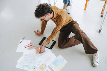 Young illustrator reviewing designs sitting on floor at office - MDOF01644